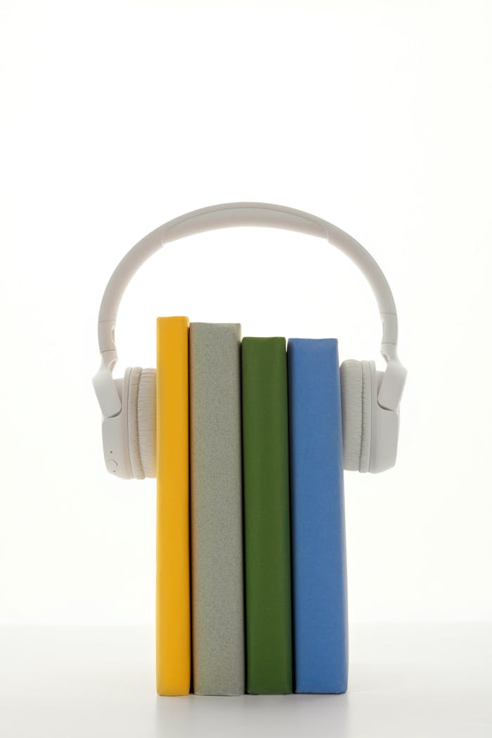 team-01 A stack of colorful books with headphones, symbolizing audio learning on a white background.